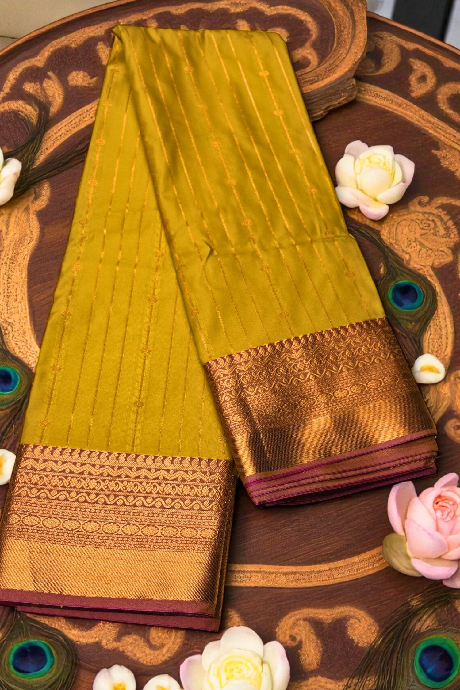 Green saree with gold border on a decorative wooden surface with peacock feathers and flowers.