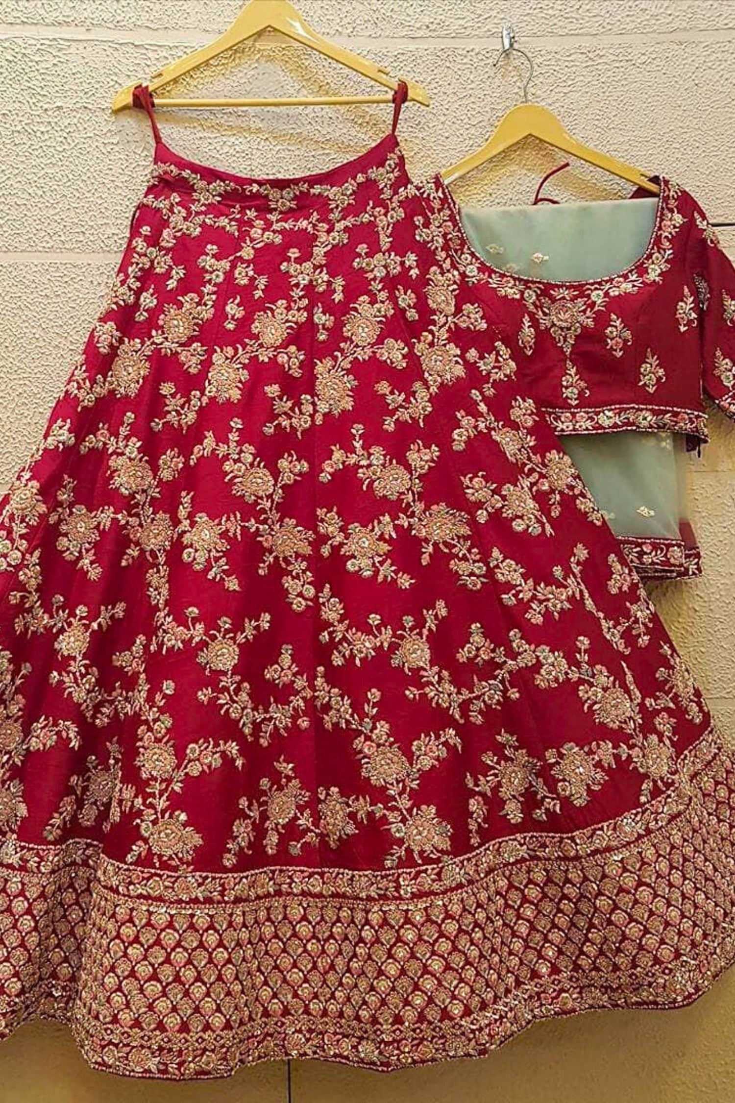 Red embroidered traditional outfit with matching blouse on hangers against a beige wall.