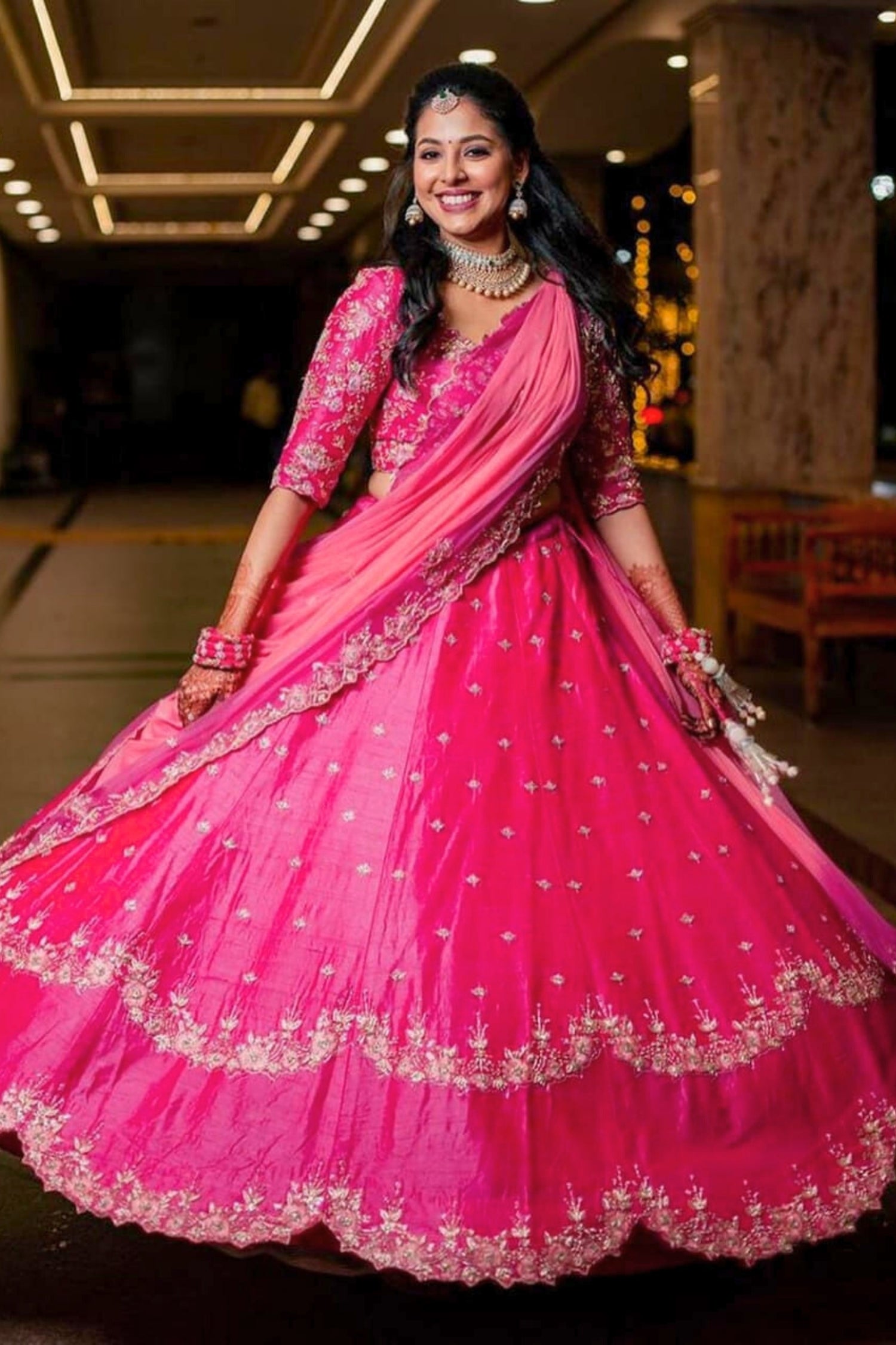 Woman in a pink traditional outfit with intricate designs indoors.