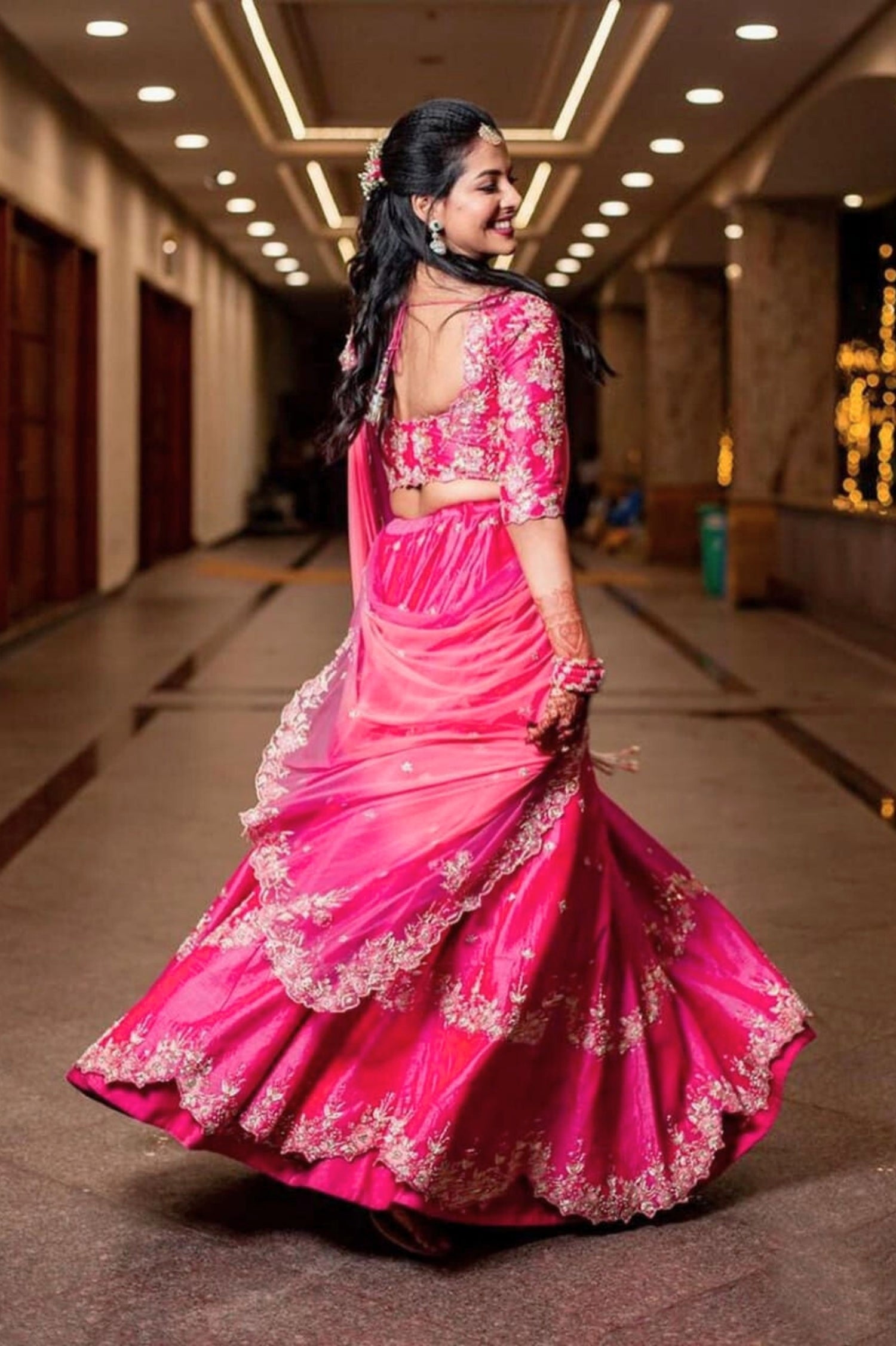 Woman in a pink traditional outfit with floral patterns in an indoor setting.