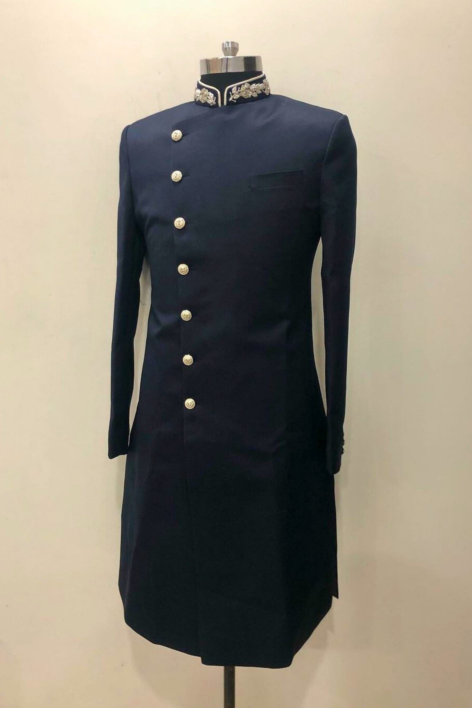 Navy blue formal coat with white buttons on a mannequin against a beige background
