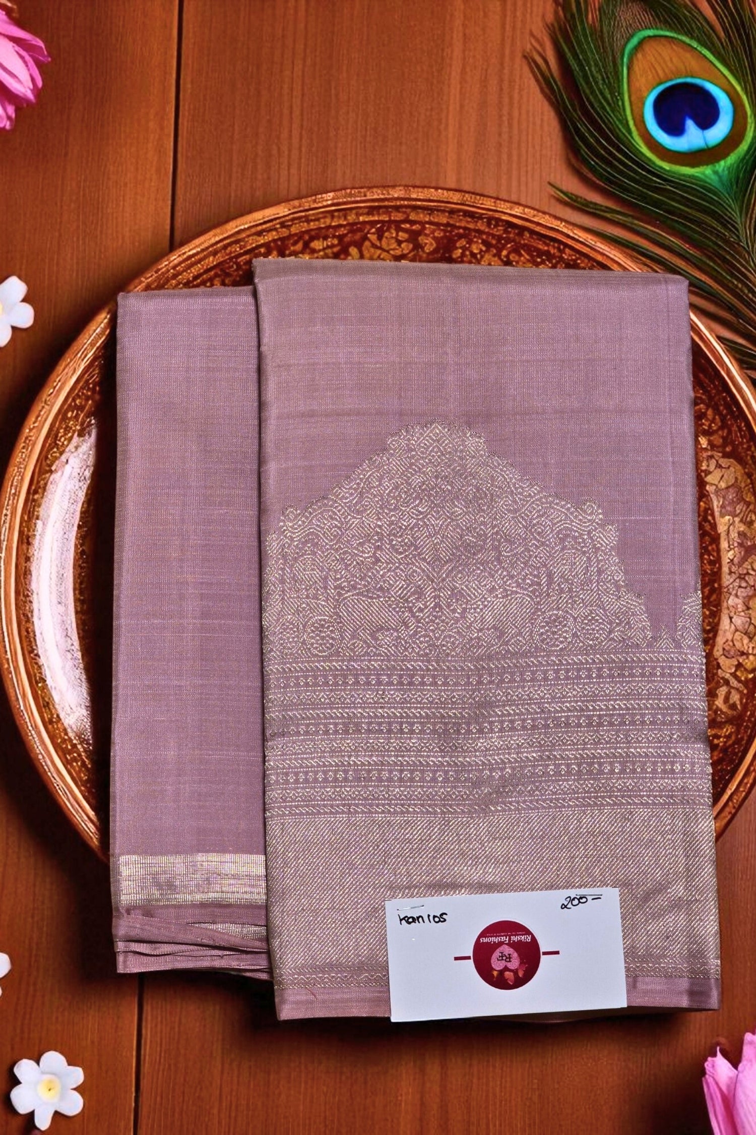 Purple saree with a white border on a wooden surface with peacock feather and flowers.