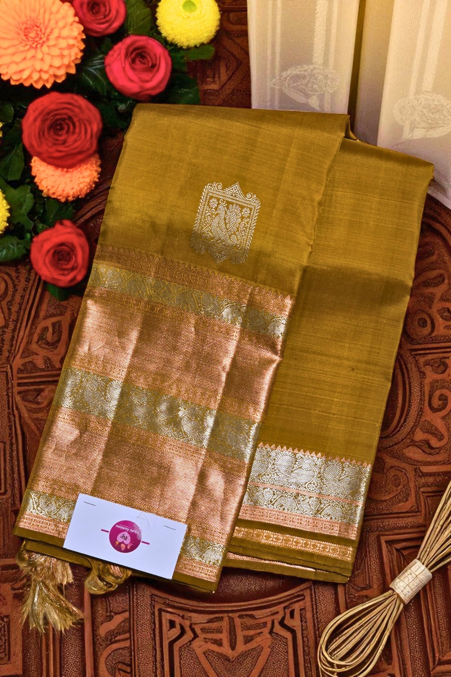 Green saree with gold border on a wooden surface with flowers and a box in the background