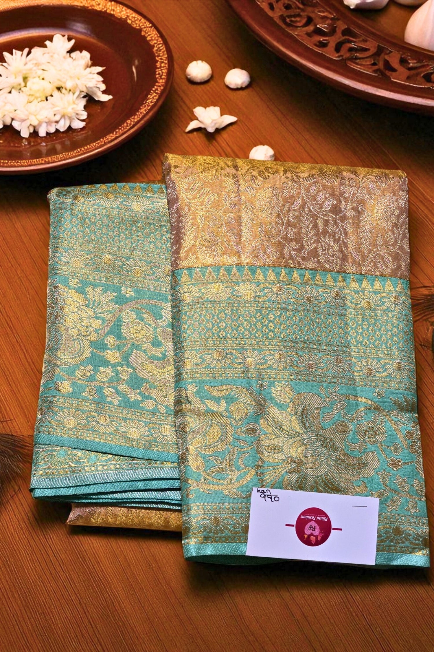 Teal and gold saree with a brand label on a wooden surface