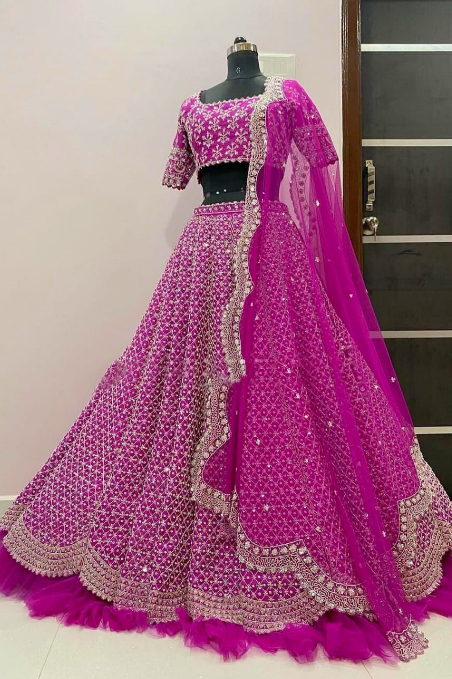 Pink embroidered lehenga on a mannequin against a neutral wall.