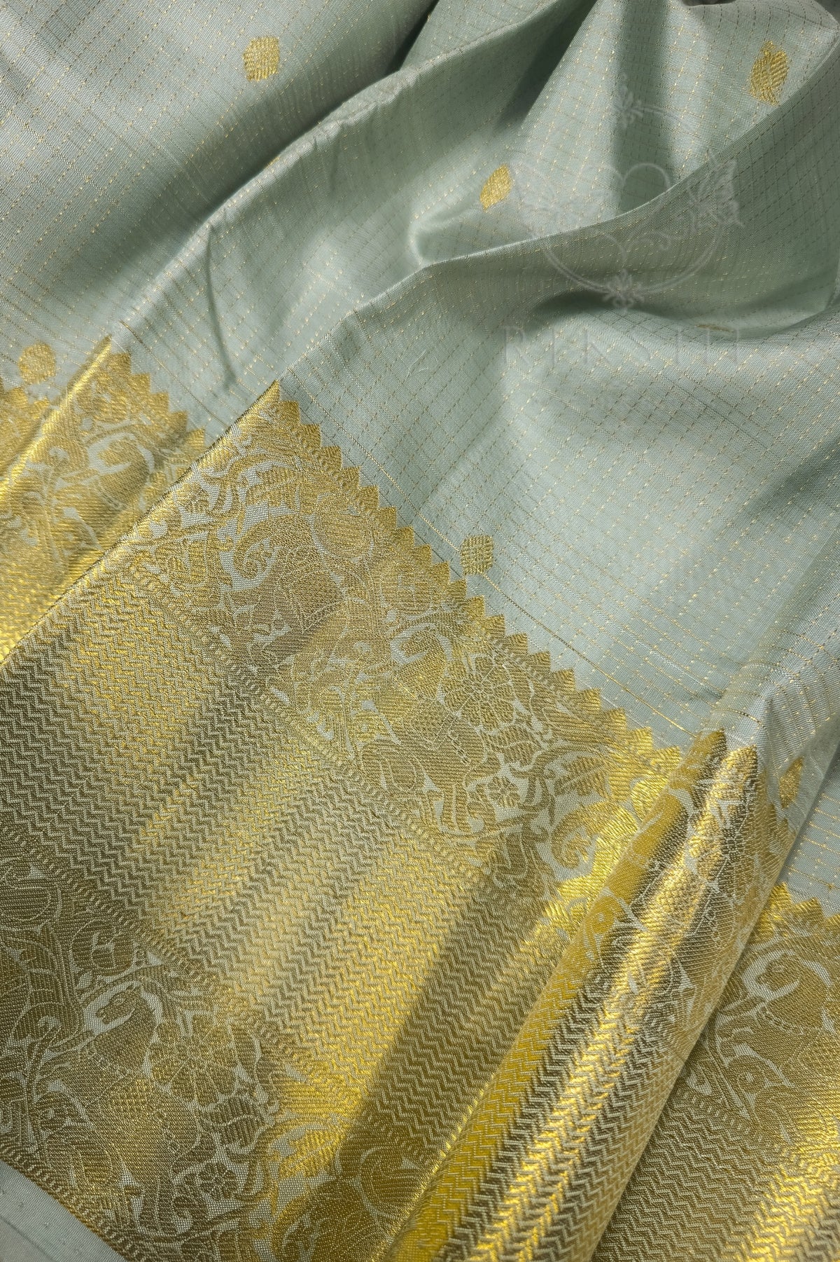 Light sage green silk saree with ornate gold zari border showcasing intricate detailing and elegant texture.