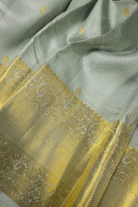 Light sage green silk saree with ornate gold zari border showcasing intricate detailing and elegant texture.