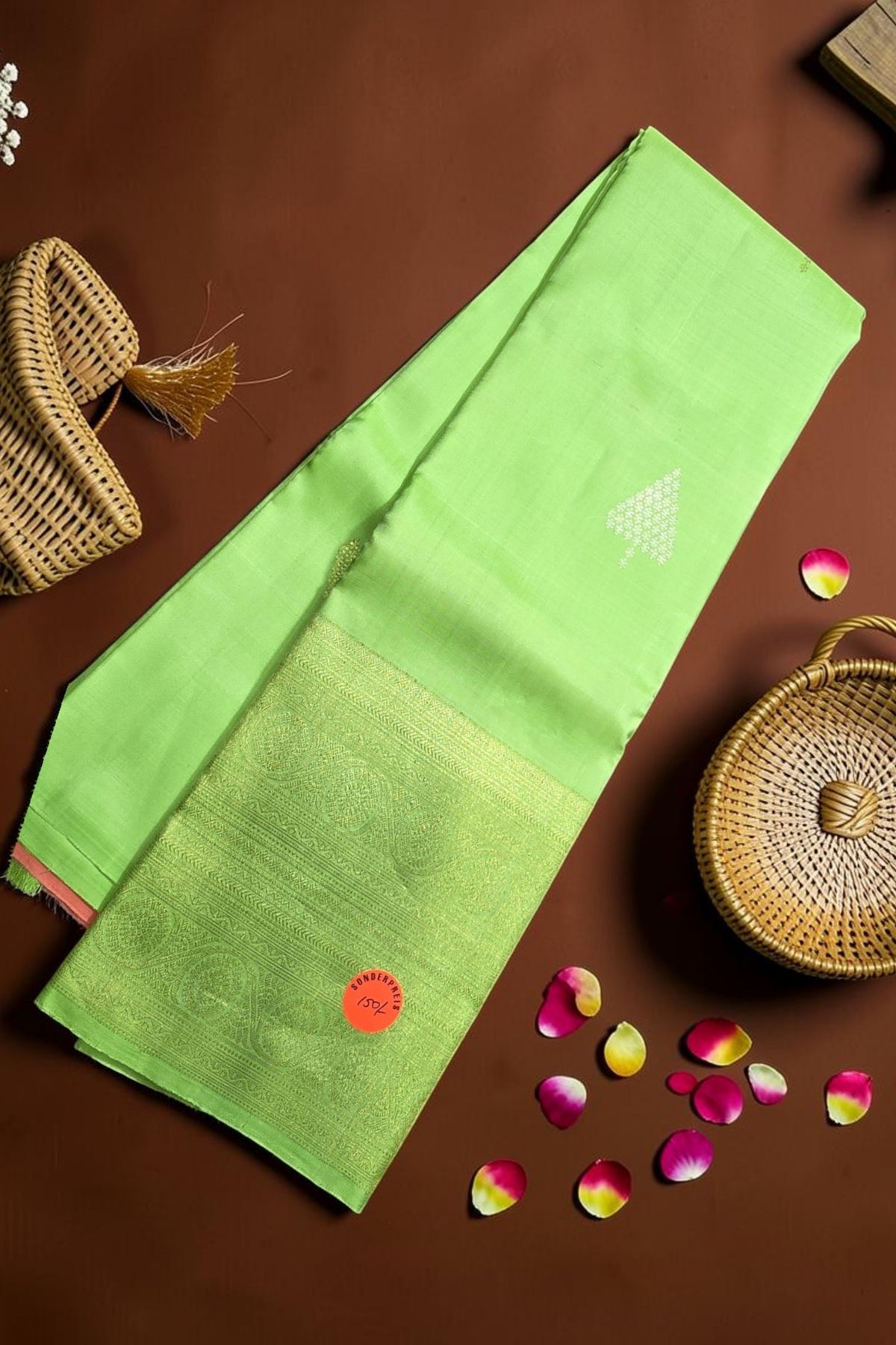 Green saree with a red flower design on a brown surface with wicker baskets and rose petals.