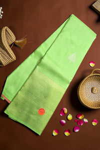 Green saree with a red flower design on a brown surface with wicker baskets and rose petals.