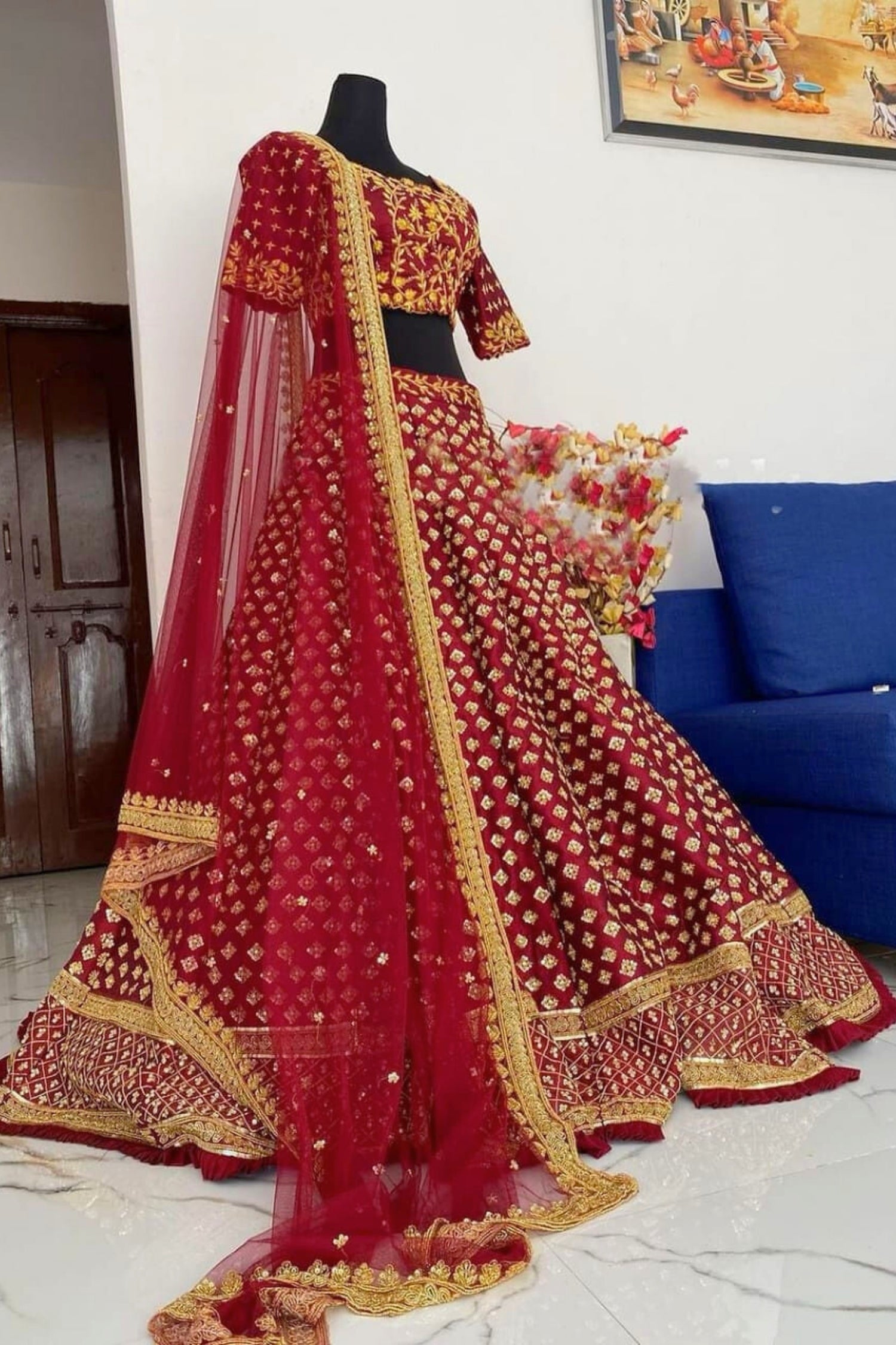 Red and gold embroidered lehenga on a mannequin against a white wall.