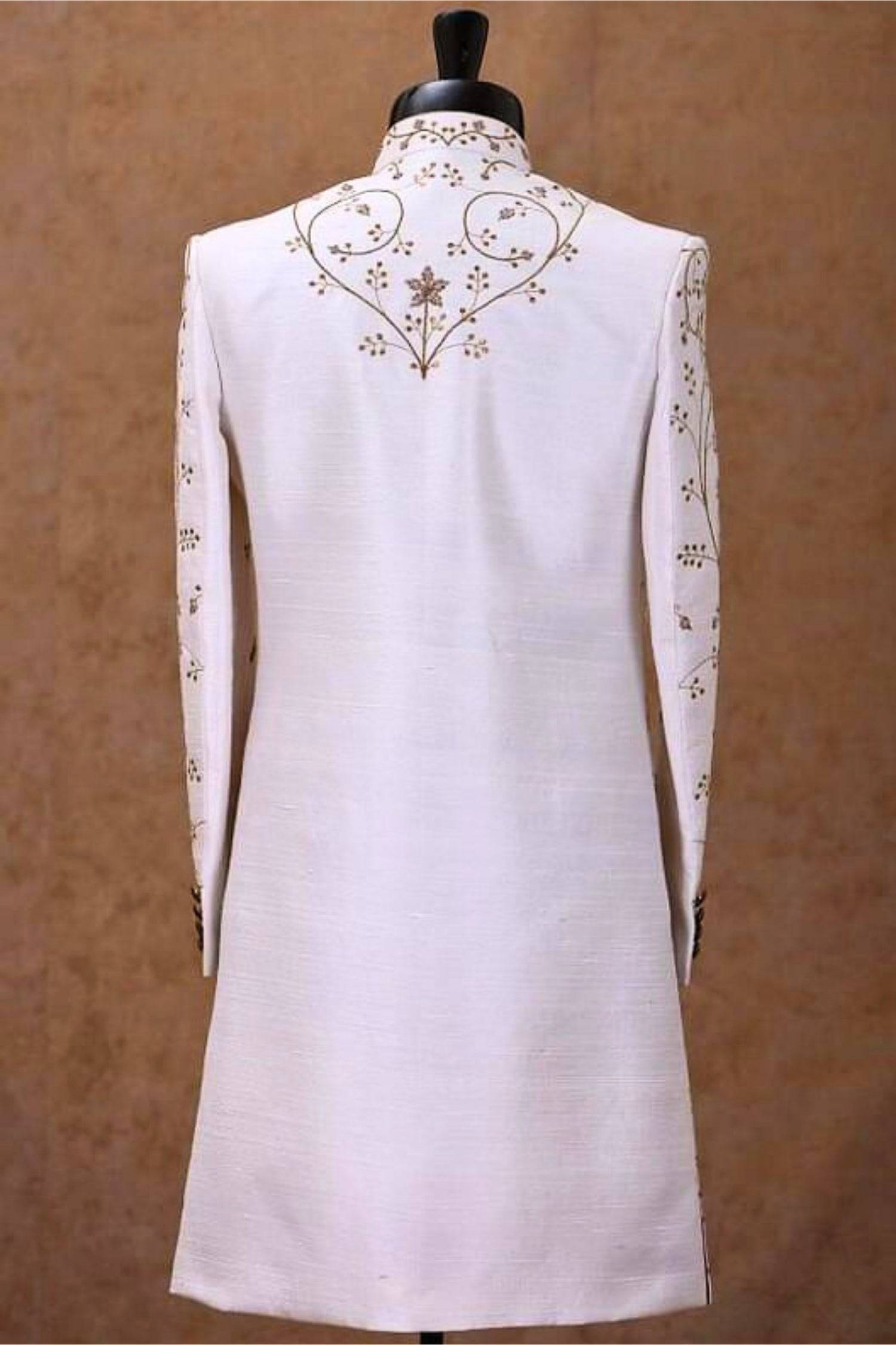 White kurta with intricate gold embroidery on a brown background