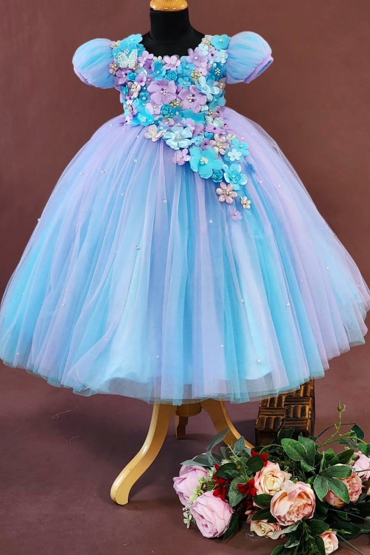Children's dress with floral embellishments on a mannequin against a brown background