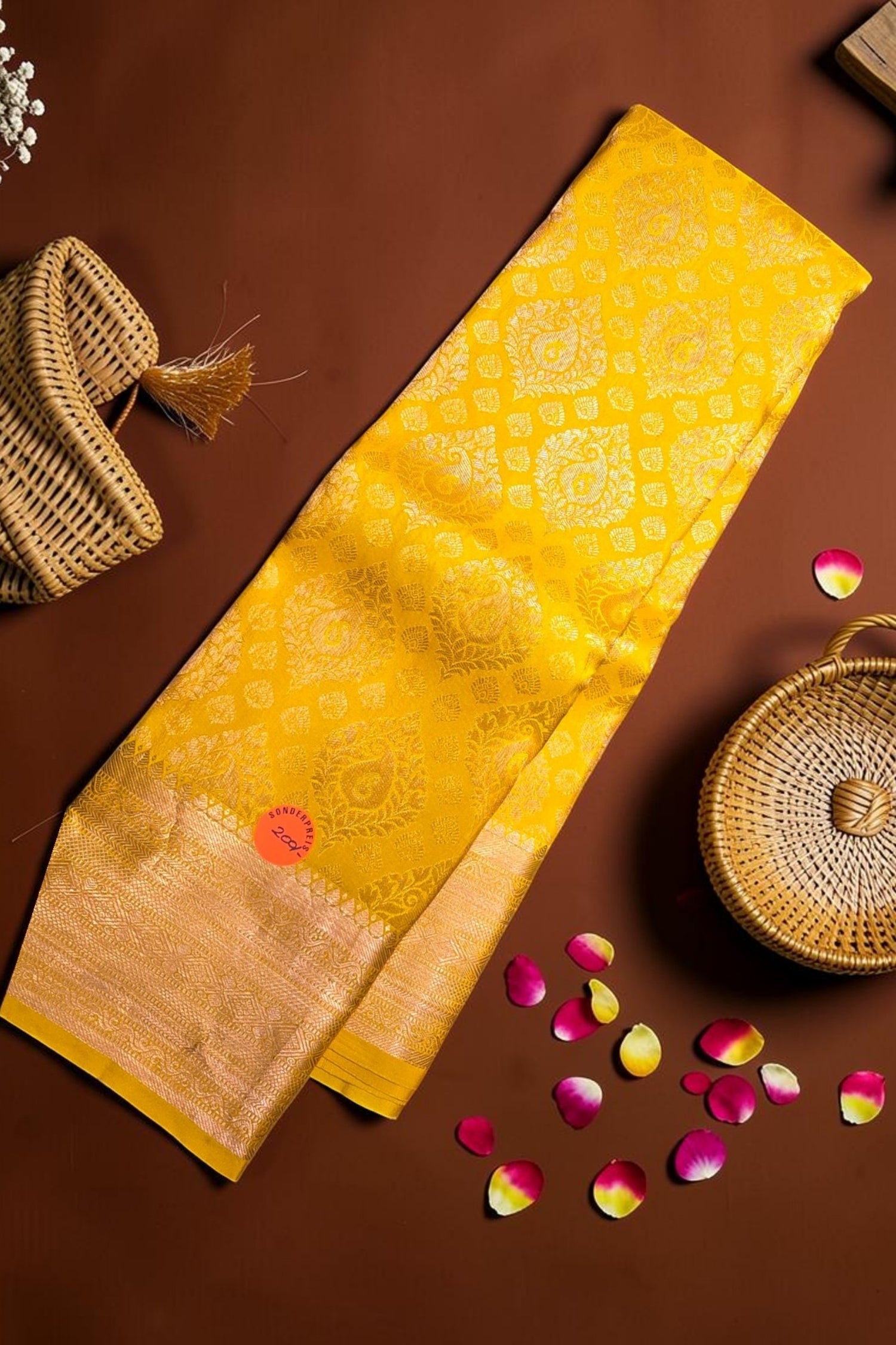 Yellow fabric with a pattern on a brown surface with wicker baskets and flower petals.