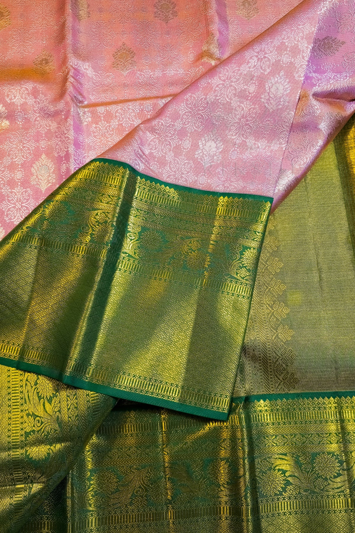 A close-up of a pink and green silk saree with intricate gold zari brocade work, showing the body fabric and the border.
