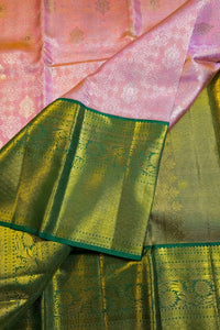 A close-up of a pink and green silk saree with intricate gold zari brocade work, showing the body fabric and the border.