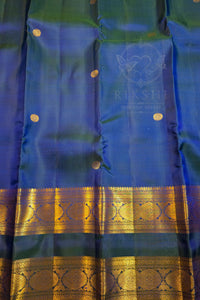 A close-up of a blue and green silk saree with gold zari borders and small gold dots, featuring a watermark logo for 'Rikshi Saffron sarees' in the center.