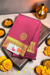 Pink saree with gold border on a wooden board, surrounded by yellow flowers and small containers.