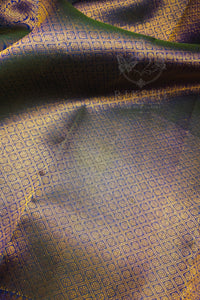 A close-up of a draped fabric with a repeating geometric woven pattern in gold and blue, showing folds and a subtle sheen.