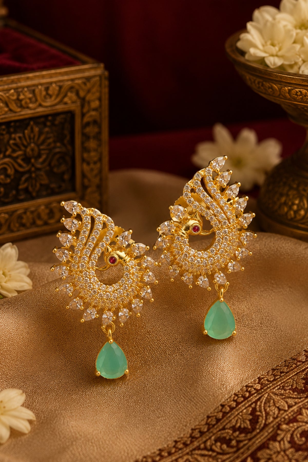Ornate gold earrings with green teardrop pendants on a textured surface.