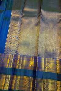 A close-up of a richly woven Indian silk saree, showcasing a metallic gold zari brocade pattern over a deep teal blue base.