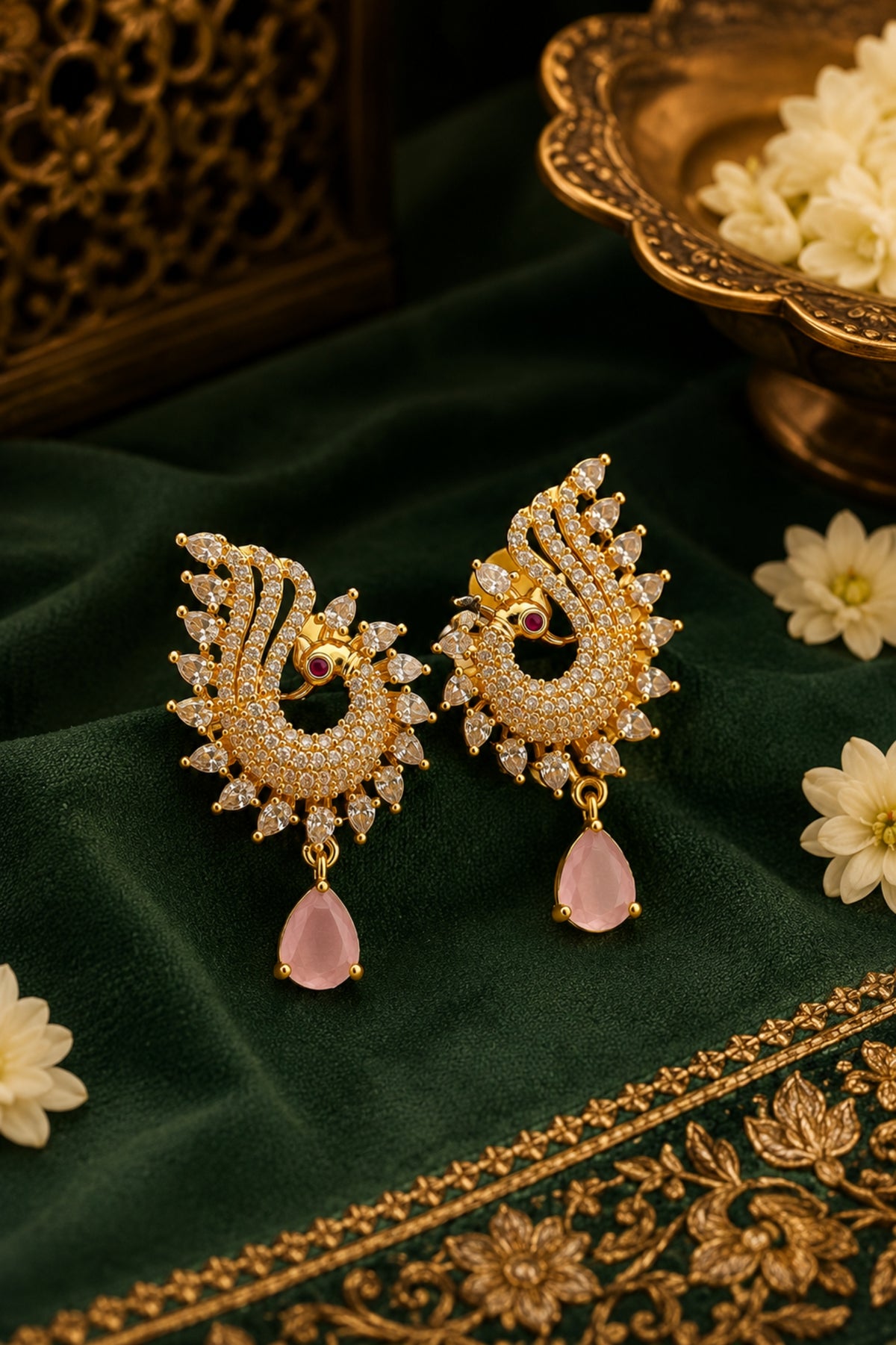 Ornate gold earrings with pink stones on a green fabric background