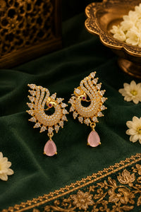 Ornate gold earrings with pink stones on a green fabric background