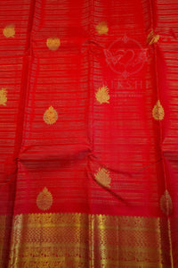 A close-up of a red silk saree with gold zari embroidery, featuring small teardrop motifs and a wide decorative gold border at the bottom. A faint watermark logo for 'Kshiti' is visible in the center.