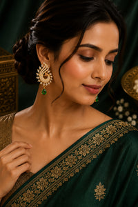 Woman wearing a green saree with gold embroidery and gold earrings.