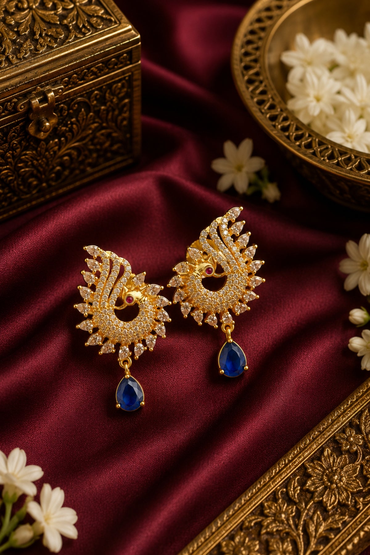 Ornate gold earrings with blue stones on a maroon fabric background