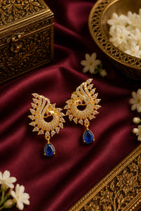 Ornate gold earrings with blue stones on a maroon fabric background