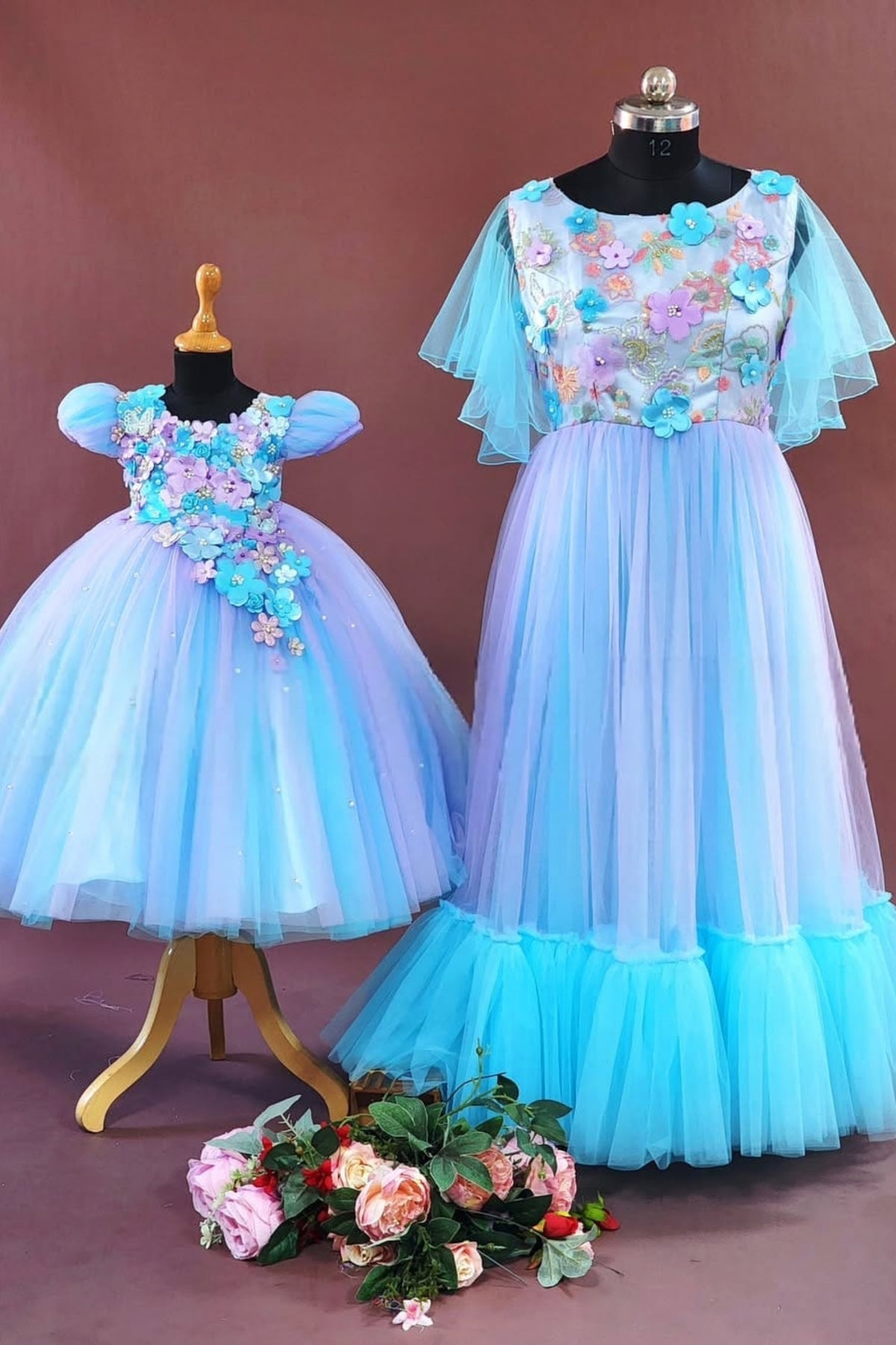 Two blue dresses on mannequins with floral details against a brown background