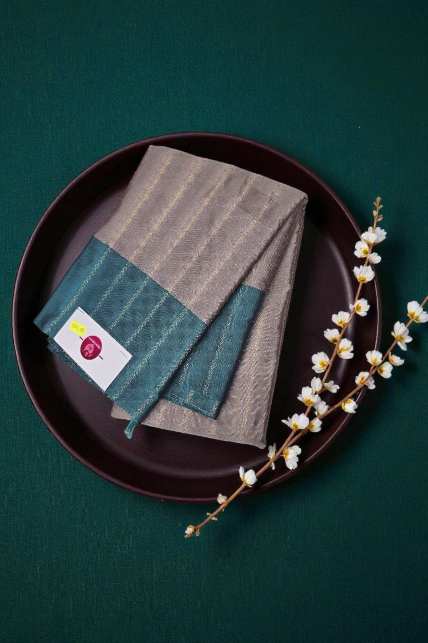 Folded gray and teal fabric on a dark plate with a branch of white flowers against a green background