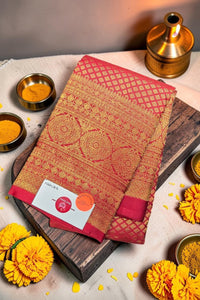 Red and gold patterned fabric with a label on a wooden board, surrounded by yellow flowers and small bowls.