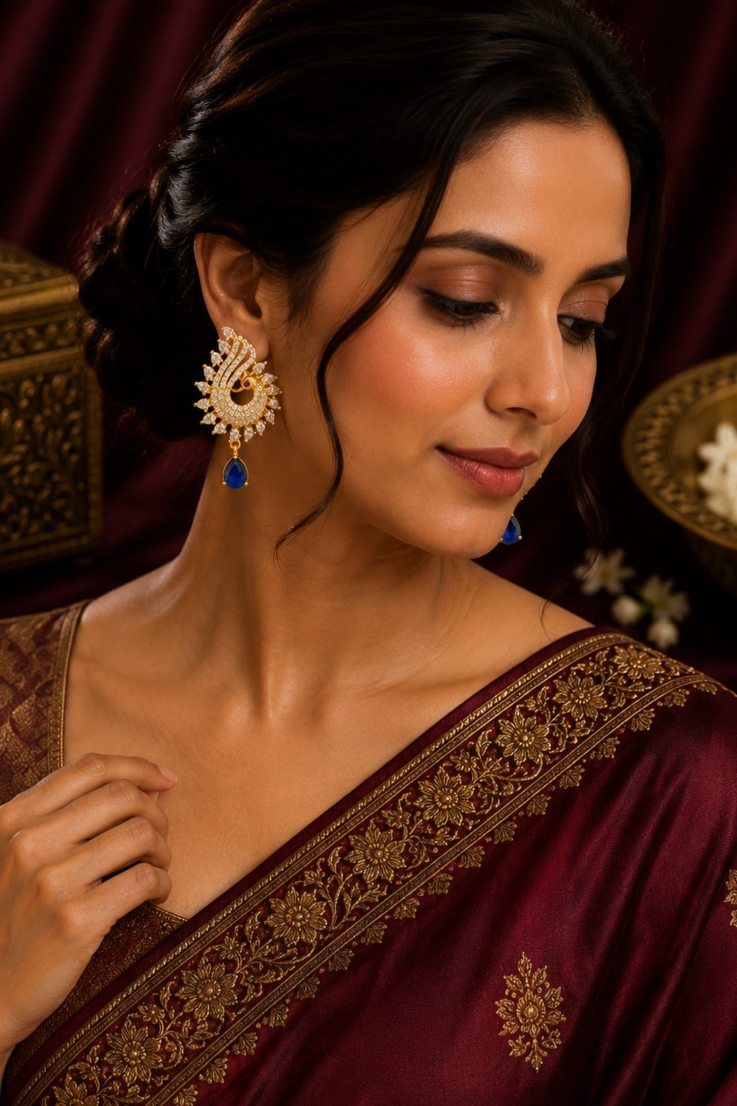 Woman wearing a maroon saree with gold embroidery and gold earrings.
