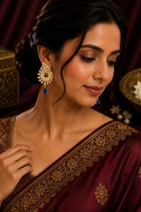 Woman wearing a maroon saree with gold embroidery and gold earrings.
