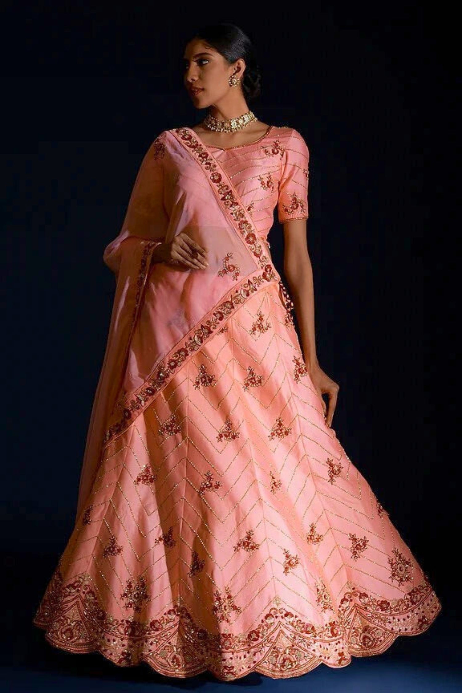 Woman wearing a traditional pink embroidered outfit with a dark background