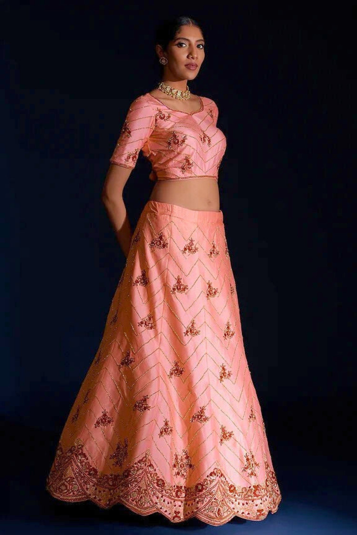 Woman wearing a pink embroidered traditional outfit on a dark background