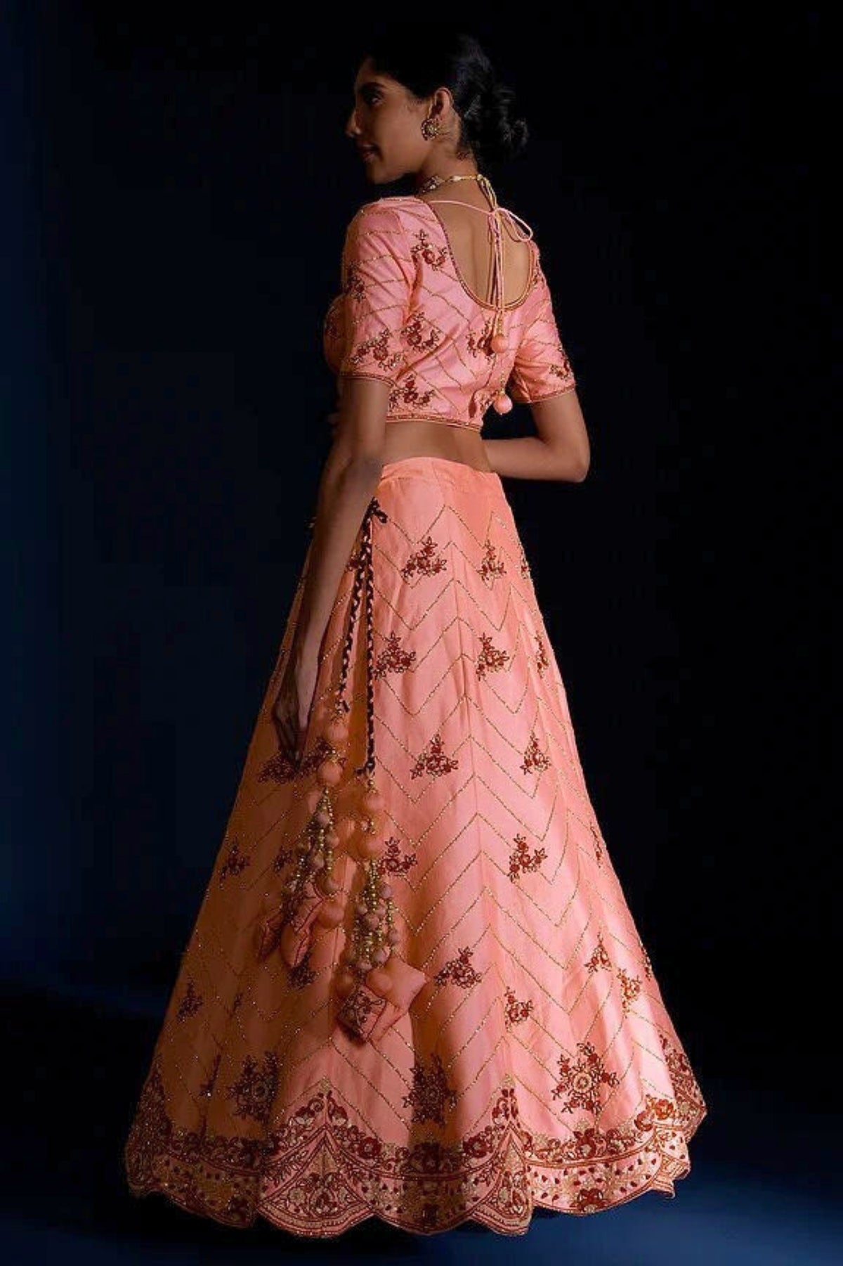 Woman wearing a pink embroidered traditional outfit against a dark background