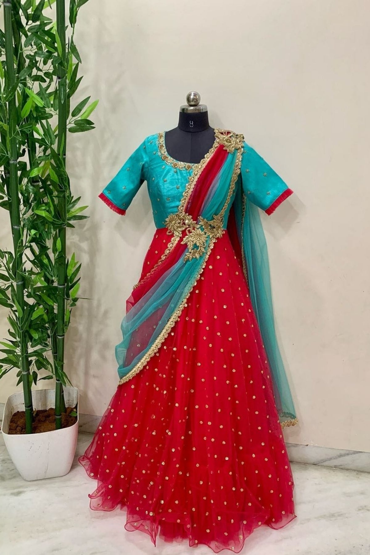 Traditional outfit with turquoise blouse and red saree on a mannequin against a neutral background.