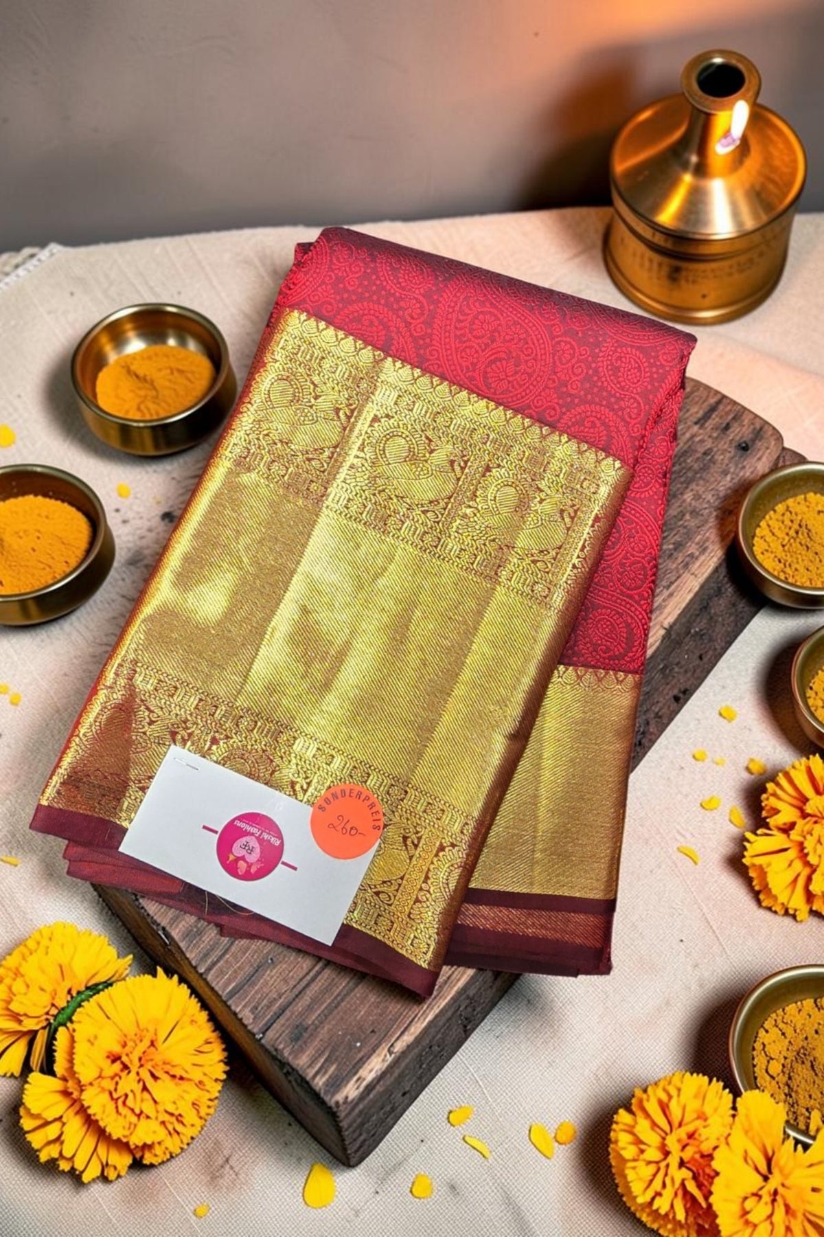 Traditional saree with a red border on a wooden board surrounded by yellow flowers and spices.
