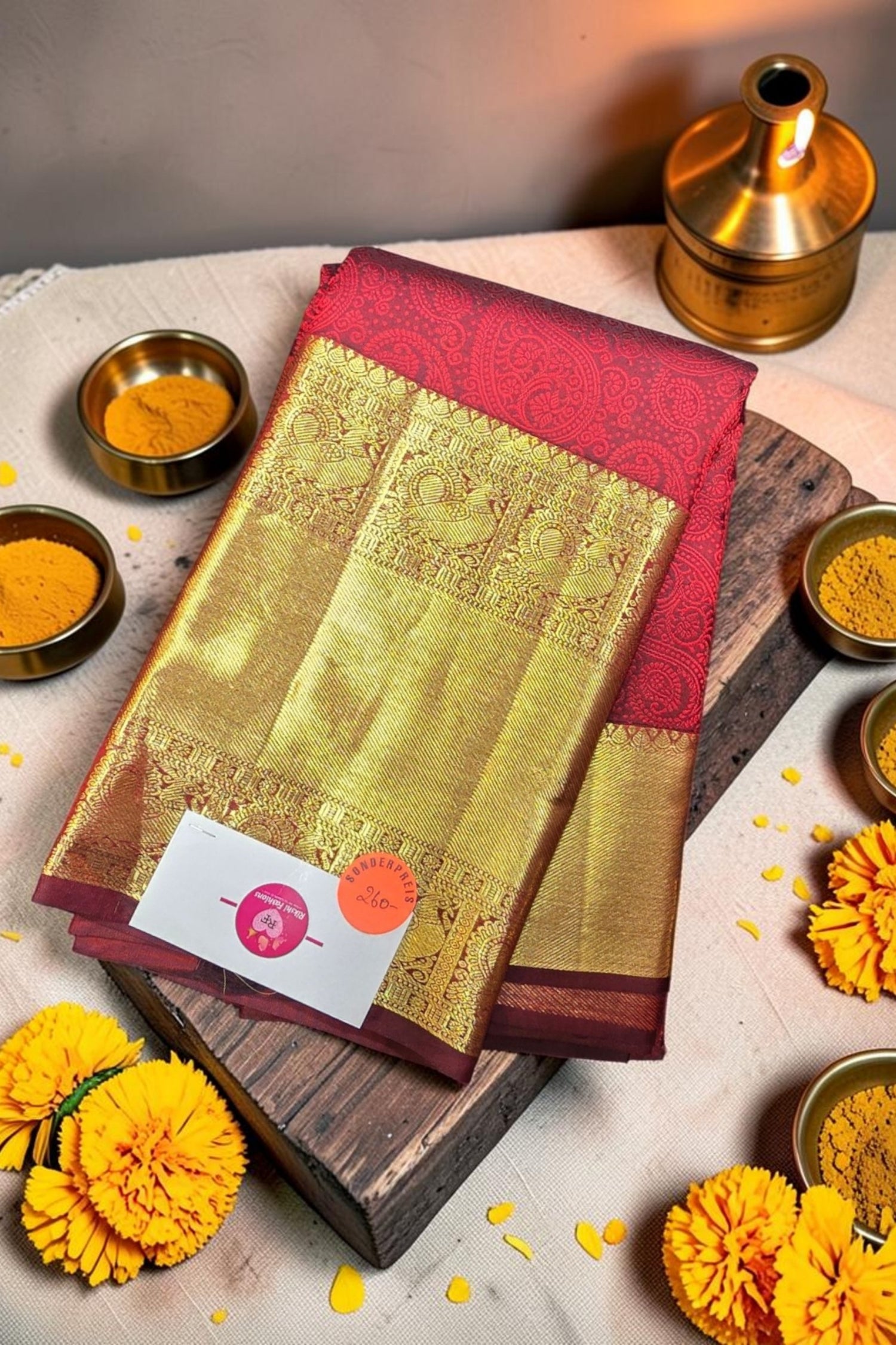 Traditional saree with a red border on a wooden board surrounded by yellow flowers and spices.