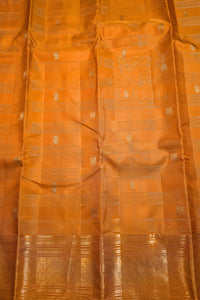 A close-up of an orange silk saree with metallic gold zari woven patterns and a wide gold border along the bottom.