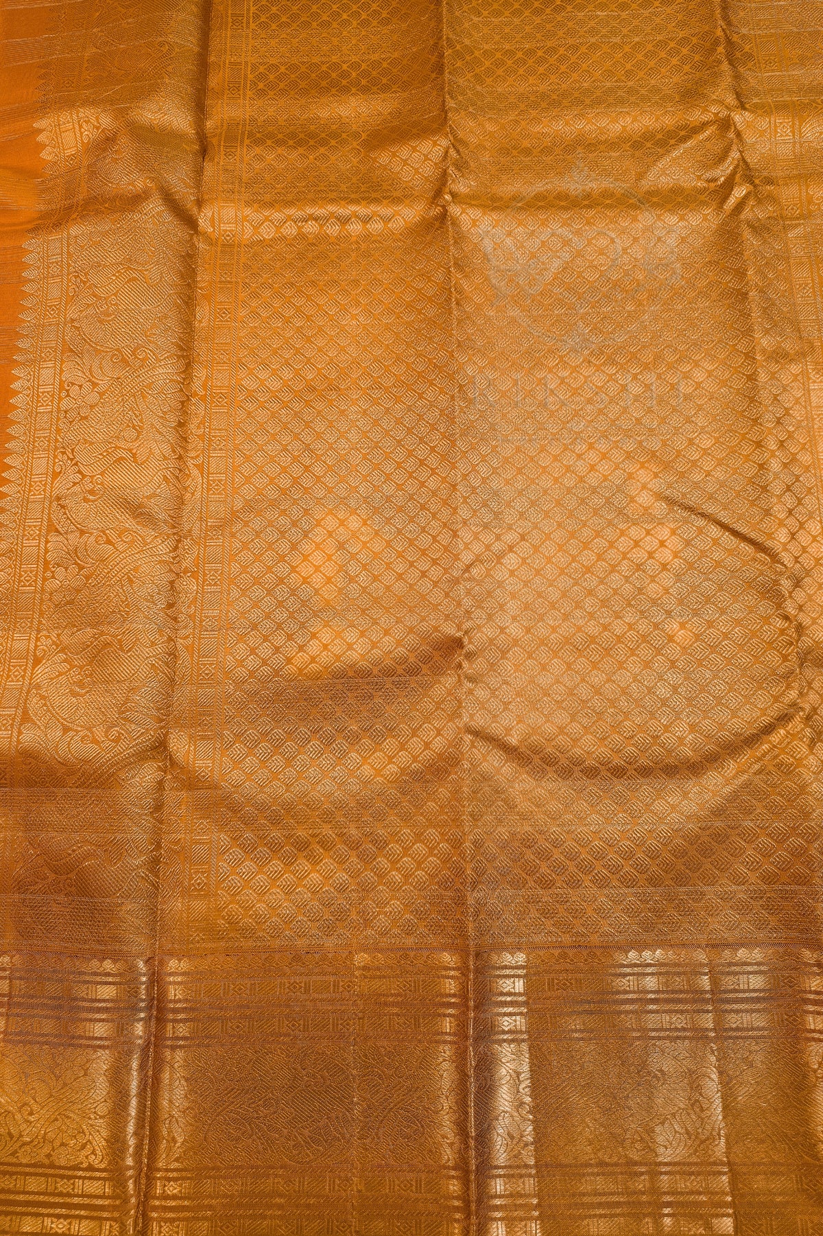 A close-up of a golden-orange silk fabric with a woven geometric pattern and a decorative border.