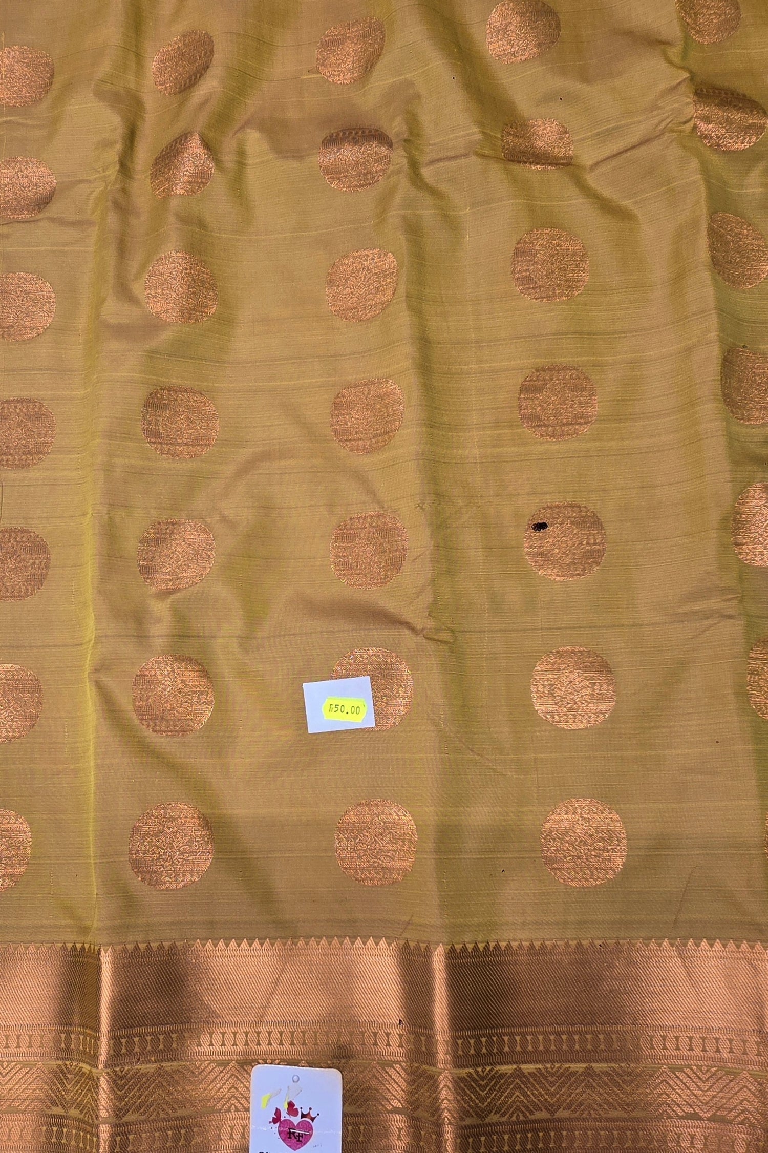 Green fabric with gold circular patterns and a brand label.