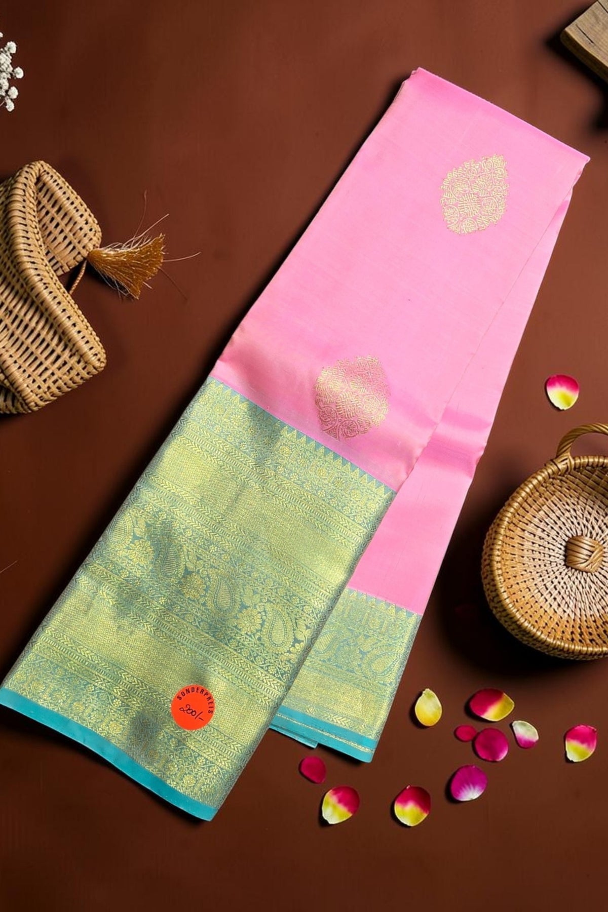 Two traditional sarees with pink and green patterns on a brown surface with decorative elements.