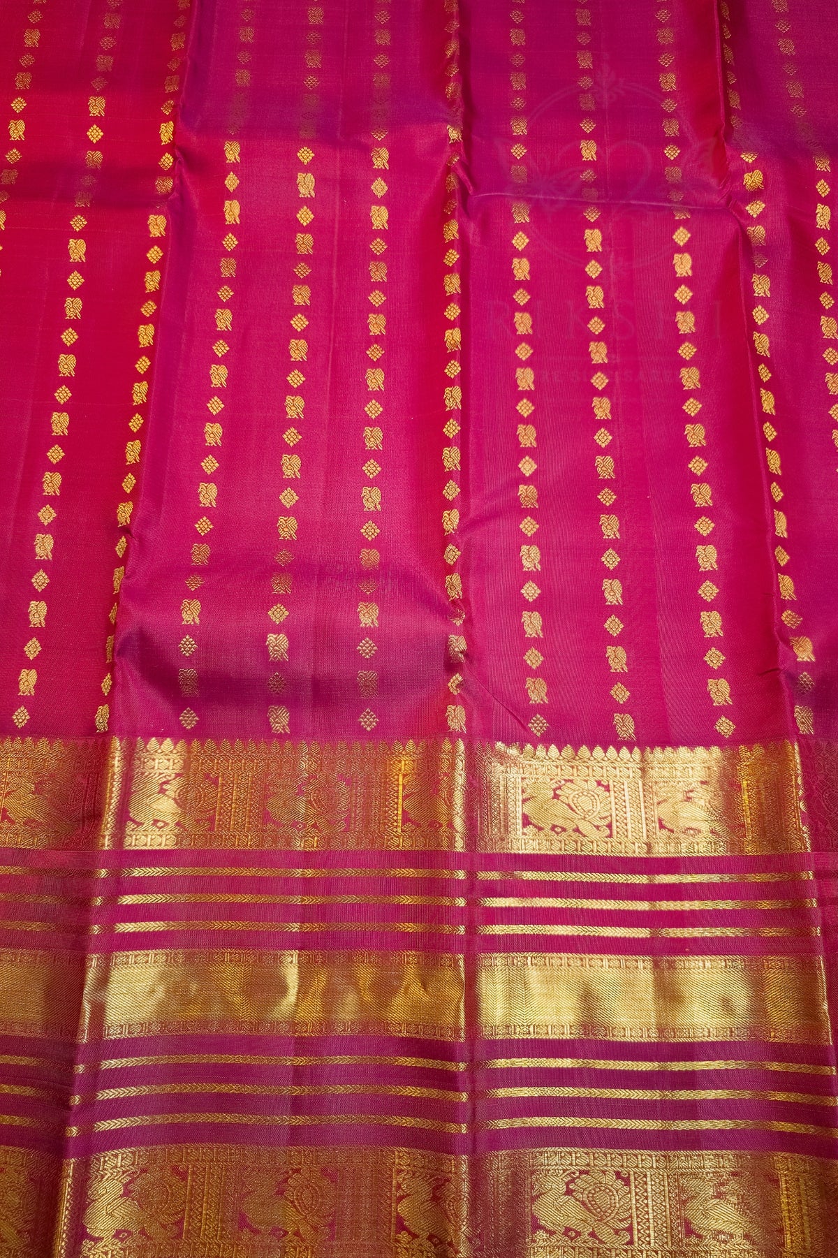 A close-up of a rich magenta pink silk saree body with vertical gold zari stripes and a wide, ornate gold zari border at the bottom.