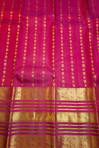 A close-up of a rich magenta pink silk saree body with vertical gold zari stripes and a wide, ornate gold zari border at the bottom.