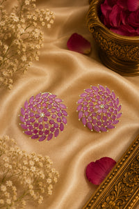 Purple floral earrings on a beige fabric background with decorative elements.