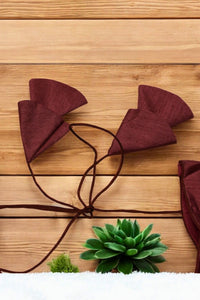 Maroon cat ears headband on a wooden surface with a green plant.