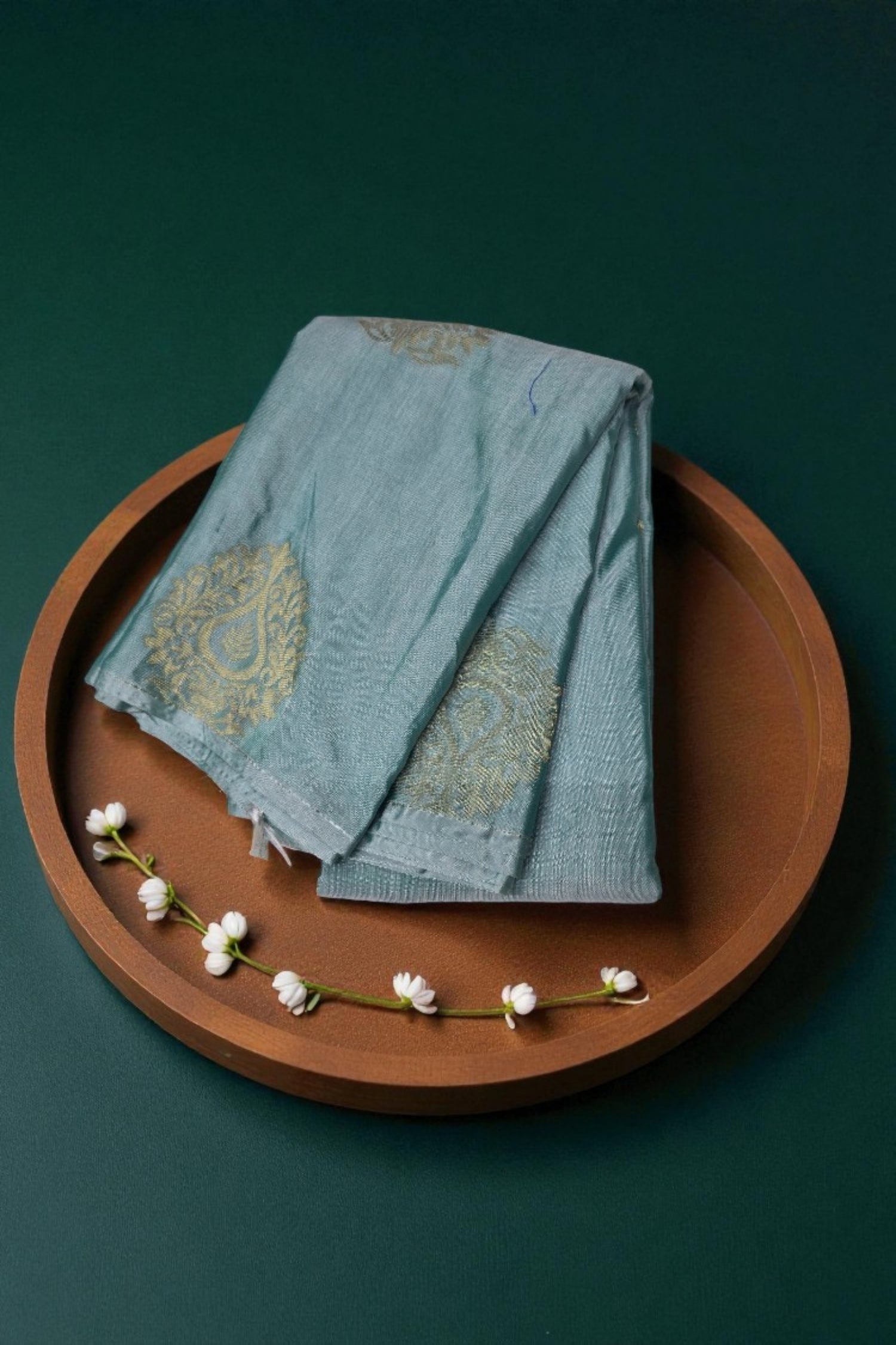 Teal fabric with gold patterns on a brown tray against a dark green background